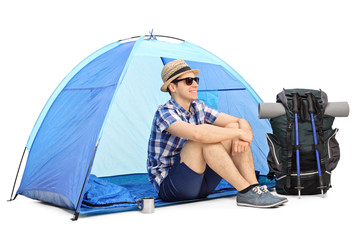 cheerful male hiker sitting in front of a tent