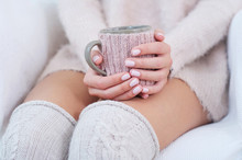 Closeup Woman Hands With Delicate Pink Manicure Holding Decorated Cup; Knitted Knee Socks On Woman Legs