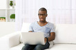 © Africa Studio - Handsome African American man sitting with laptop on sofa in room