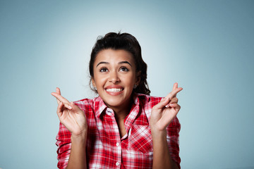 Waiting for the moment. Portrait of beautiful young mixed race woman keeping fingers crossed and looking up while standing against isolated background.