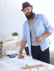 Wall Mural - Portrait of male designer in hat with blueprints at desk 