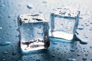 Two clear melting ice cubes with drops around, close up