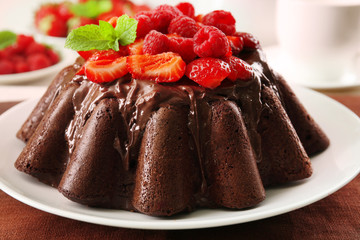 Tasty chocolate muffin with glaze and berries on table close up