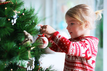 Little Girl Decorating Christmas Tree With Toys And Baubles. Cute Kid Preparing Home For Xmas Celebration.