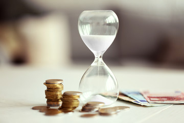 Wall Mural - Hourglass with money on table on bright background