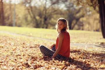 Wall Mural - girl sits resting in a park on the fallen leaves