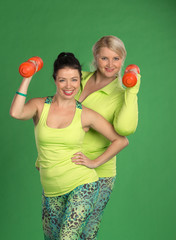 Woman team pumping up muscules with dumbbells on green backgroun