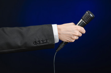 Business speech and topic: a man in a black suit holding a black microphone on a dark blue background in studio isolated