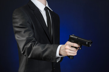 Firearms and security topic: a man in a black suit holding a gun on a dark blue background in studio isolated