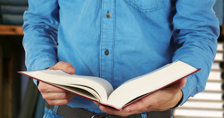 Poster - Male hands holding open book on bookshelves background