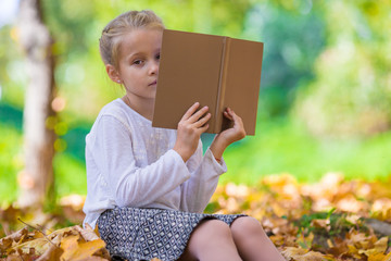 Wall Mural - Adorable little girl reading a book in beautiful autumn park 