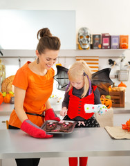 Wall Mural - Halloween dressed girl with mother holding tray with biscuits