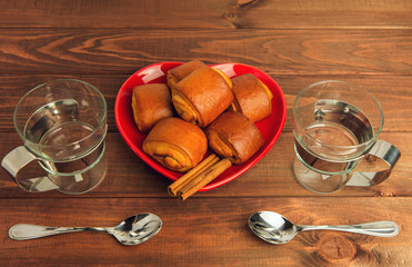 Two empty glass cups with metal handles and cinnamon rolls on a