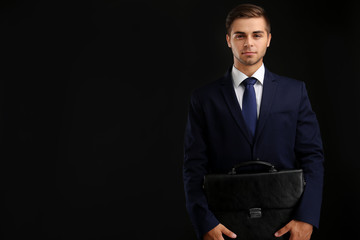 Wall Mural - Elegant man in suit with briefcase on dark background