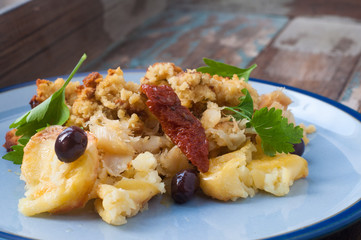 Bacalhau broa. A Portuguese Brazilian dish of salt cod baked with crumbled corn bread, olive oil and olives. Garnished with sun dried tomatoes and parsley.