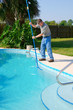 © Michael O'Keene - Residential pool cleaning service man working on a sparkling clean pool brushing the side clean