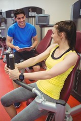 Wall Mural - Fit woman using weights machine with trainer