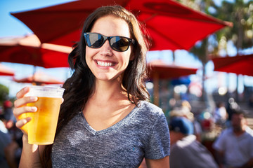 portrait of happy woman holding cup of beer outside on sunny day