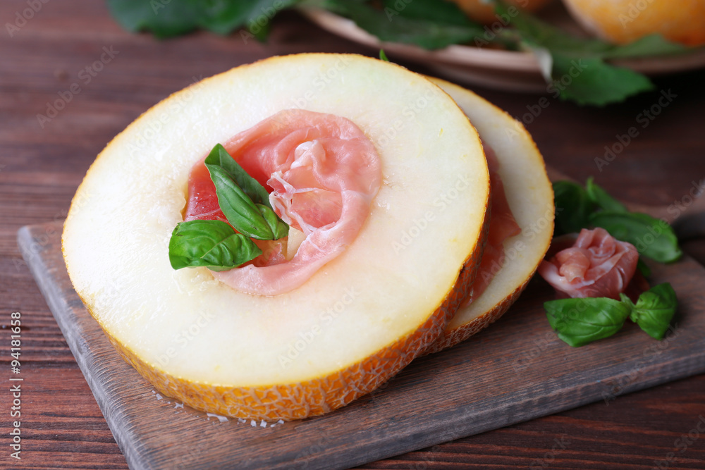 Melon with prosciutto of Parma ham on wooden table, closeup