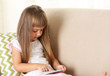© Africa Studio - Beautiful little girl  with smart phone sitting on sofa, on home interior background