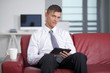 © COSPV - Smiling young businessman holding a tablet at sofa in office sit
