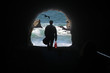 A silhouette of a  man walking through a tunnel onto the beach with crashing waves.