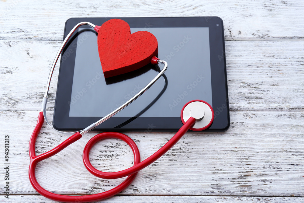 Red rubber stethoscope with black tablet and heart on wooden background