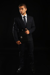 Wall Mural - Elegant man in suit with briefcase on dark background