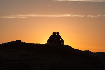 Silhouette of Couple sitting on a rock near the sea and watching the sunset