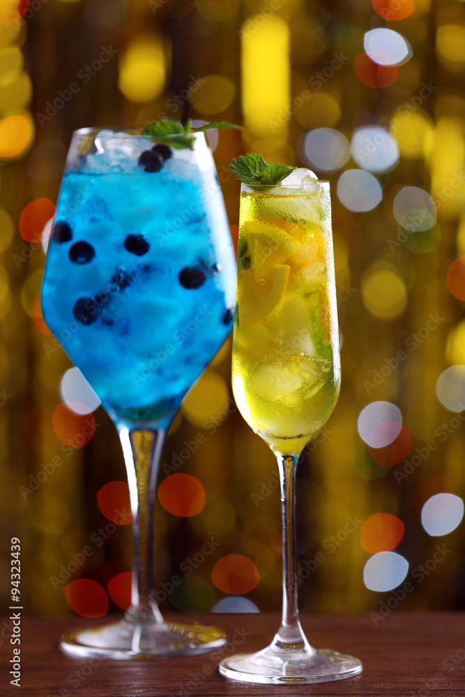 Glasses of cocktails with ice on blurred lights background