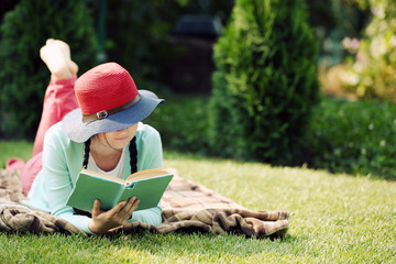 Wall Mural - Young woman with book lying on green grass outdoors