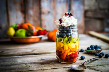 Wall Mural - Colorful fruit salad in a jar on rustic wooden background