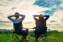 Couple Sitting In Chairs And Admire The Sunrise Over The City