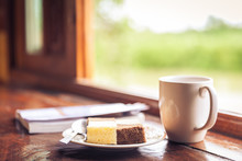 Cake And Cup Of Coffee On Wooden Table Near Window Sill. 