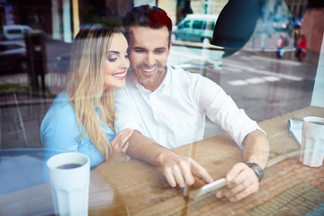 Wall Mural - Happy couple at cafe using smartphone