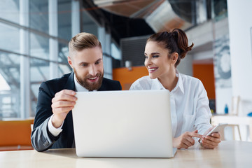 Canvas Print - Two cheerful business people working with laptop at office