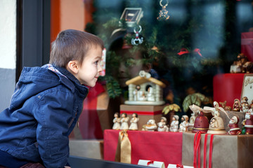 Sweet little boy, looking through a window in shop, decorated fo