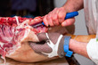 A man wearing protective gloves cuts fresh bacon and beef with a metal butcher knife in a meat industry setting.