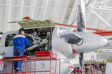 Engineer Aviation Plant Repair Jet Engines In Aviation Hangar. Aircraft Under Heavy Maintenance. Technician In Blue Working Uniform