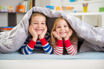 Two happy children lying under blanket