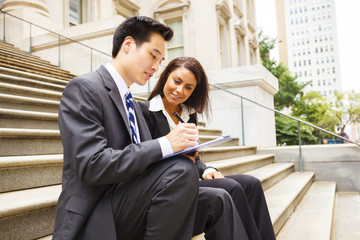 Two well dressed people sitting on steps working together outdoors. Could be legal or business professionals.