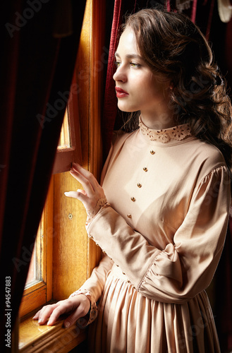 Young woman in beige vintage dress of early 20th century standin