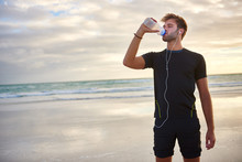Fit Young Man Drinking From A Water Bottle On The Beach