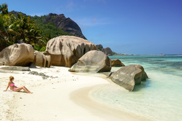 Beautiful young woman in paradise beach of Seychelles in la Digue island, Anse Source d'Argent. Boulders black granite rocks, turquoise water, white sand and blue sky.