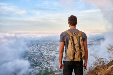 Wall Mural - Young man looking at the city from a mountain trail