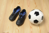 Fototapeta Sport - Balón de fútbol y botas en el suelo de madera