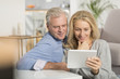 © Atelier 211 - Mature couple sitting in sofa and using tablet pc