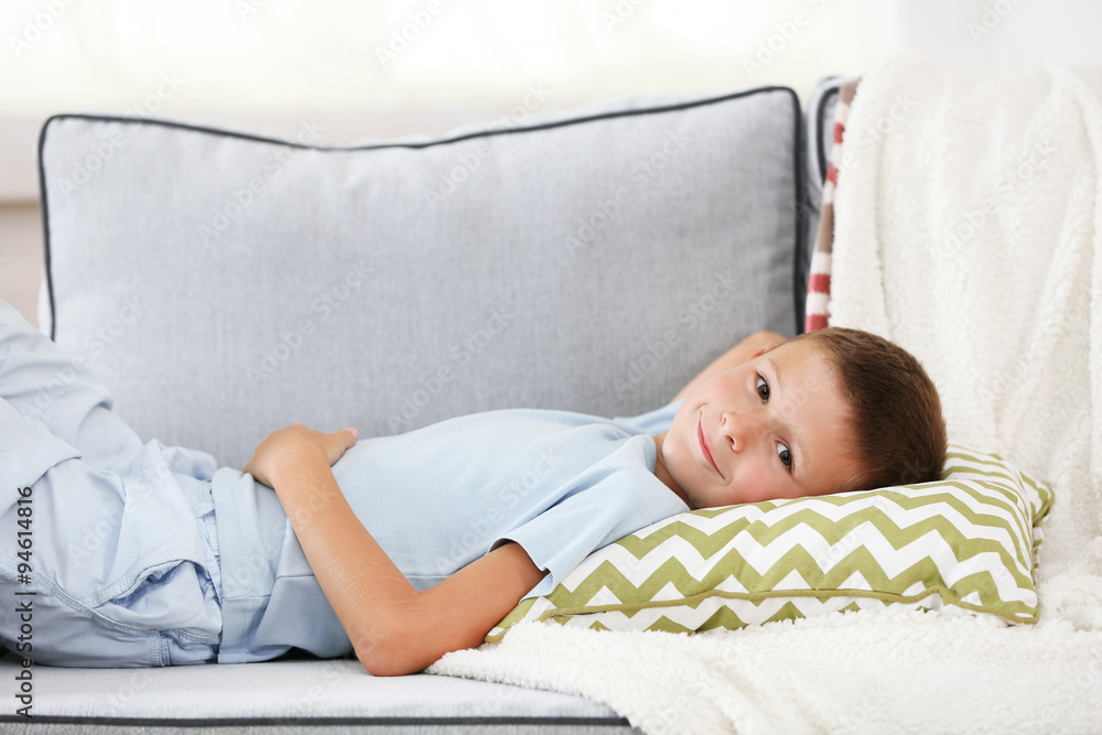Little boy sitting on sofa, on home interior background