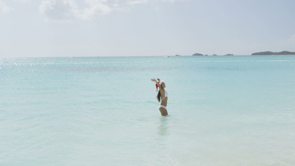 Wall Mural - Christmas beach girl in santa hat on travel happy laughing having fun running joyful and cheerful smiling excited. Woman on Christmas vacation holidays getaway on white sand Caribbean beach. RED EPIC.