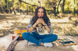 © kegfire - Adorable teenager girl wearing casual clothes having a picnic on autumn day in forest. Cute and beautiful hipster young woman smiling and holding a cupcake, sitting on blanket by guitar.